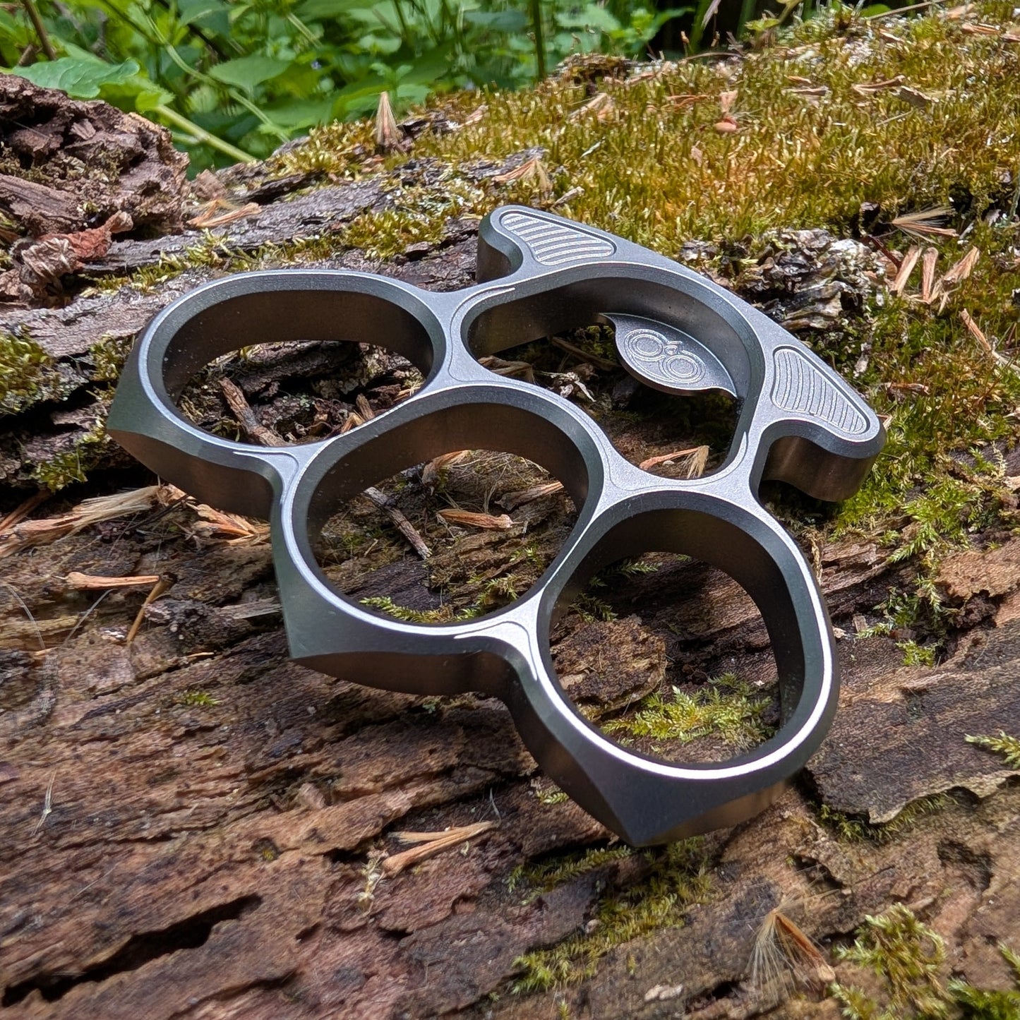 titanium bottle opener on a wooden surface with greenery in the background