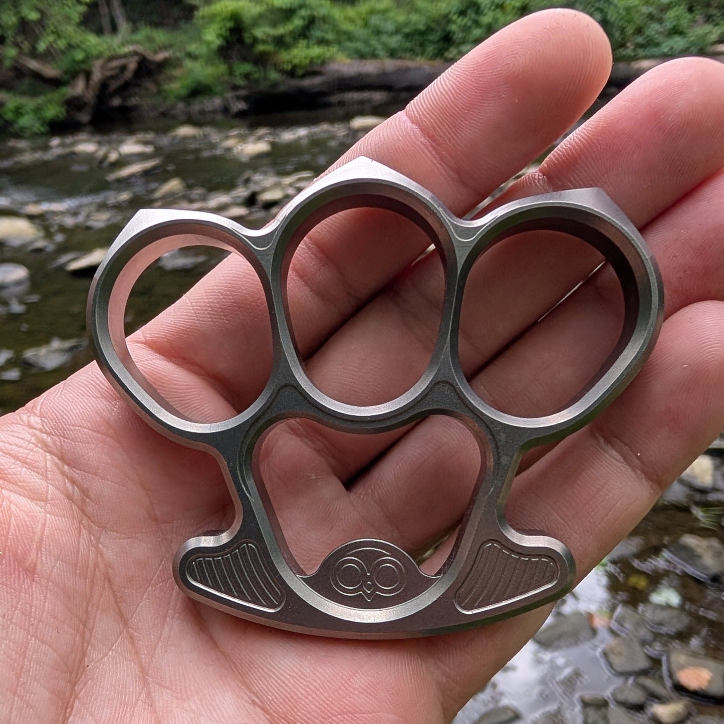 titanium bottle opener held in a hand with a natural background
