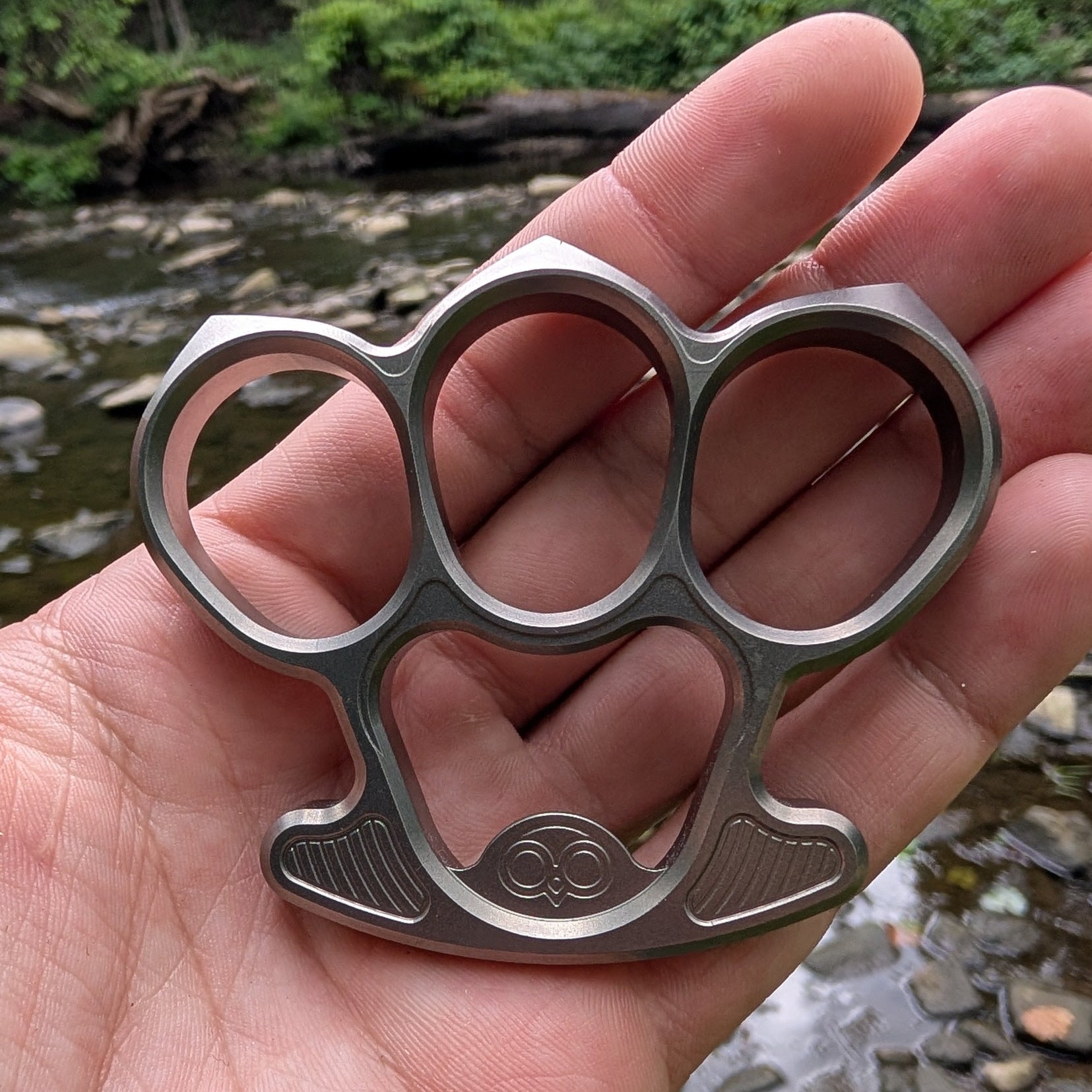 titanium bottle opener held in a hand with a natural background